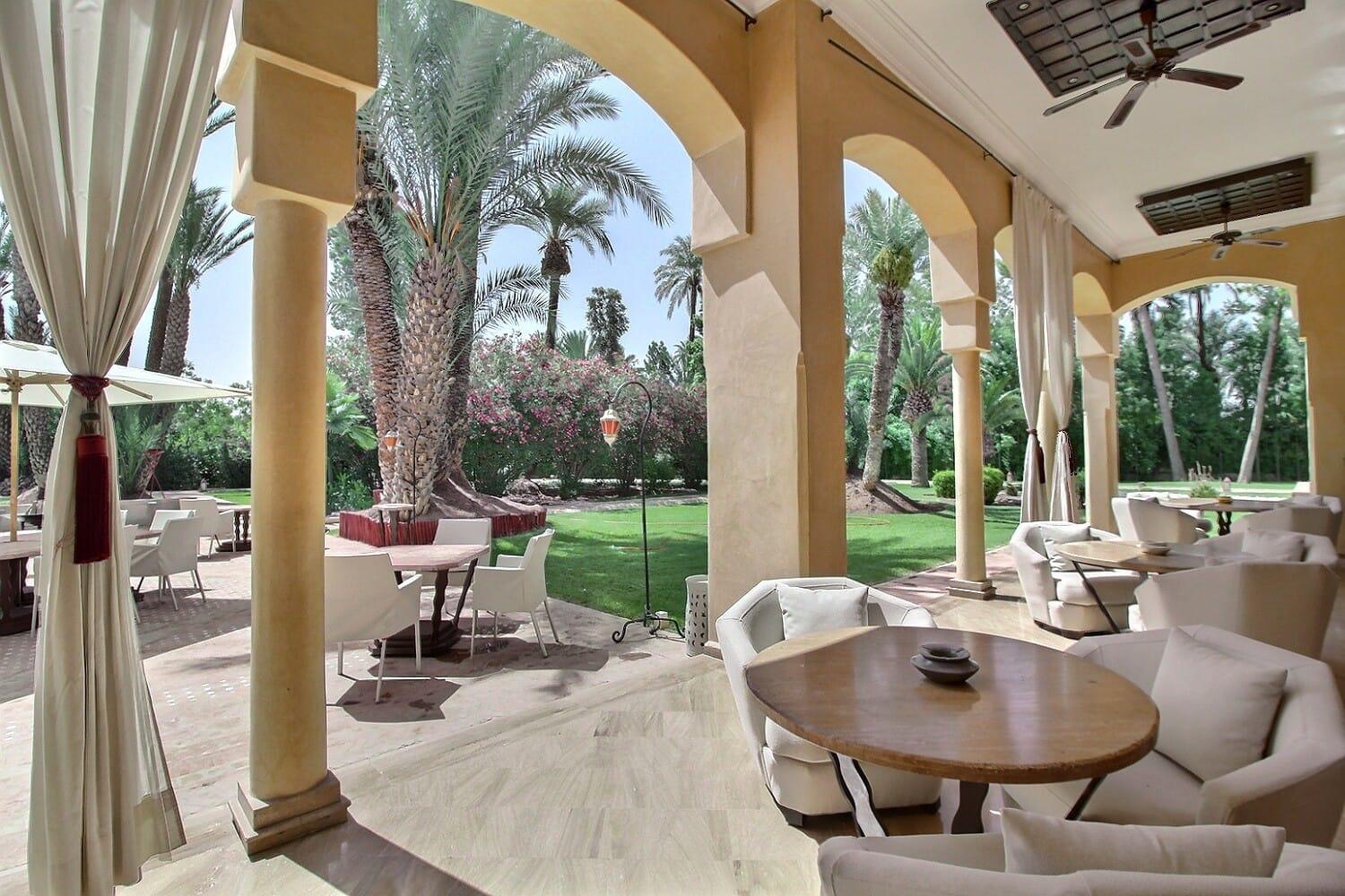 The covered terrace of The Palais Monte Carlo — white armchairs under the arches, opening onto the garden
